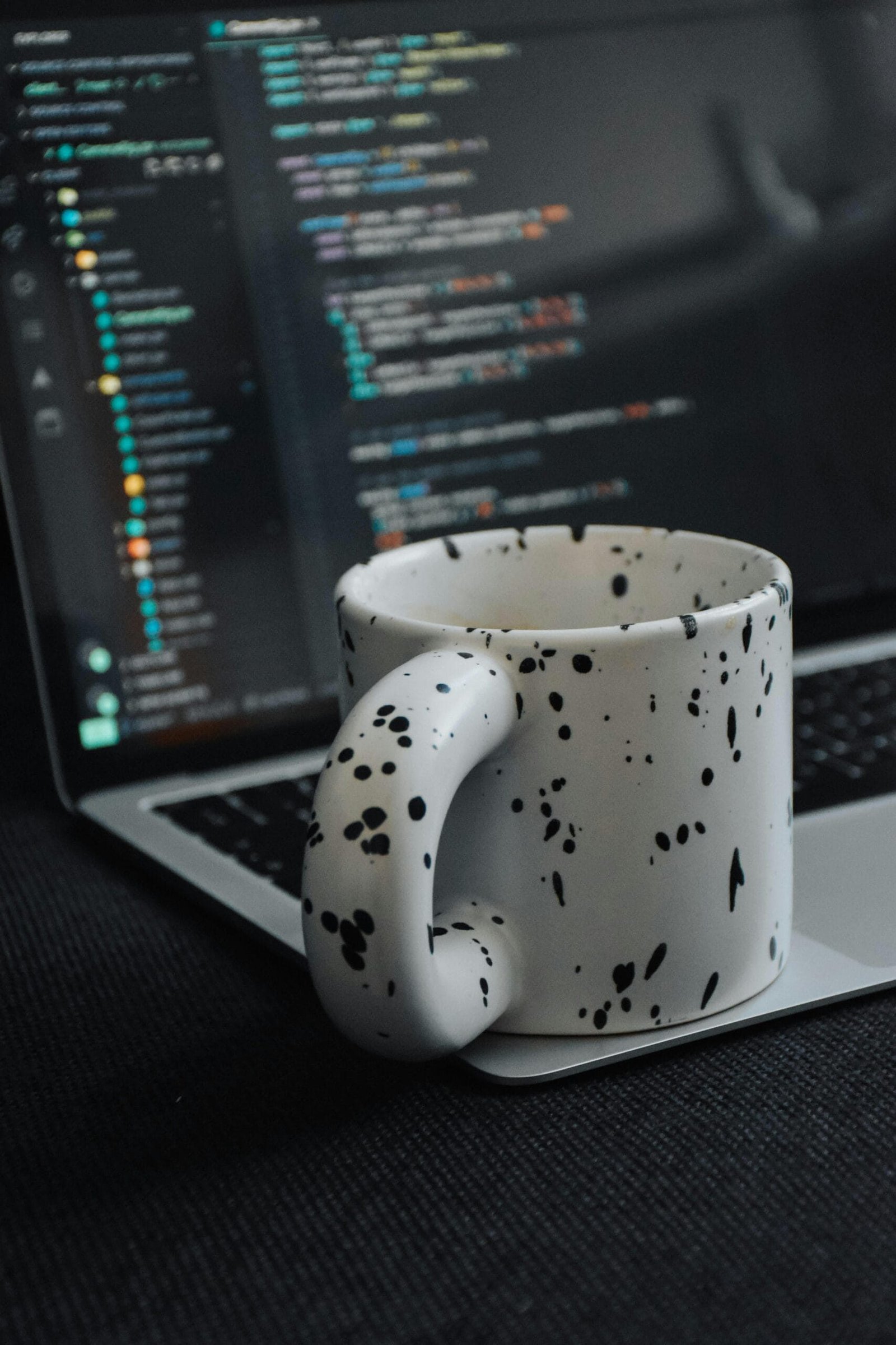 Speckled coffee mug on a laptop with visible code, creating a coding workspace vibe.