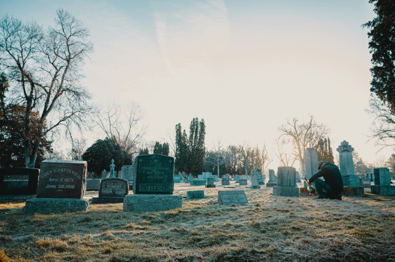 A serene cemetery at sunrise with a person reflecting by a gravestone